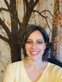 a woman in a yellow shirt smiling in front of a tree